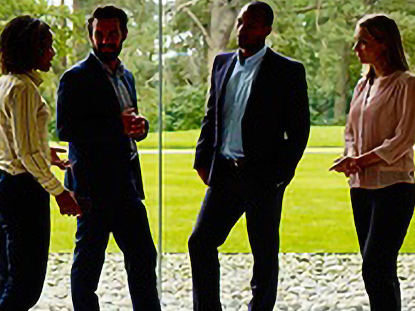 Group of employees having a conversation in an office lobby overlooking a lush green garden