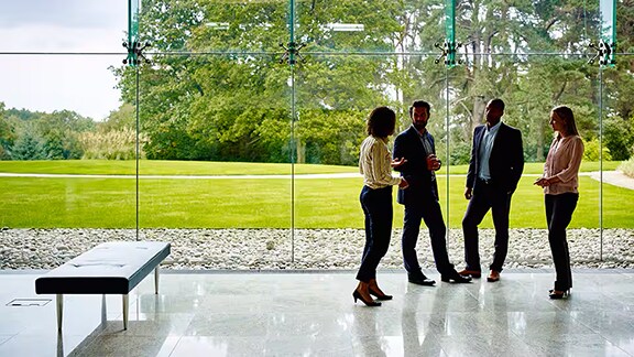 Group of employees having a conversation in an office lobby overlooking a lush garden