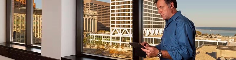Man working on a tablet standing next to a window overlooking a city