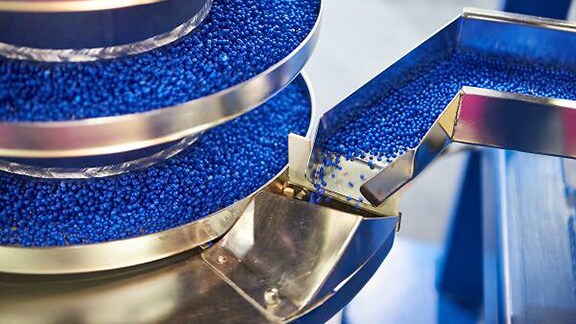 Blue plastic granules being poured into steel rows