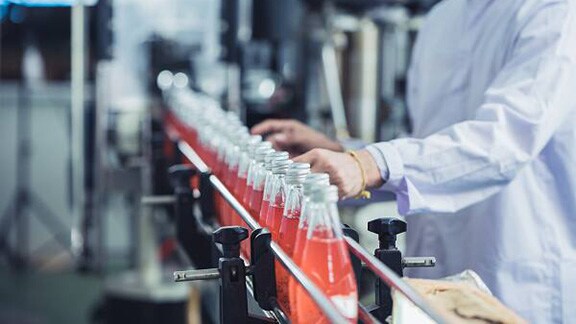 A food safety worker examining rows of bottles of juice on a conveyor belt
