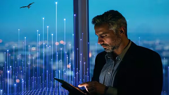 Man working on a tablet near a glass wall overlaid with graphics of transmission nodes
