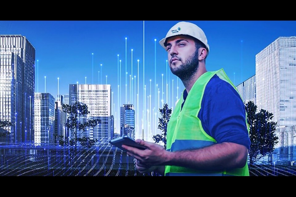 A Johnson Controls worker in a safety helmet and vest walking outdoors with a tablet with graphics of transmission nodes in the background