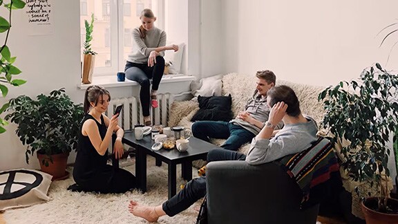 Four friends hanging out in a grey-themed living room decorated with houseplants