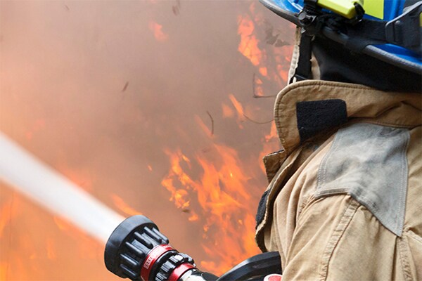 Two firefighters in safety suit dousing a flame using water hose