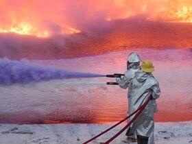 Two firefighters in safety suit dousing a flame using water hose