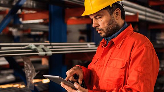 A man wearing a safety helmet working on a tablet in a warehouse