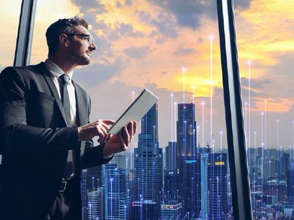 Businessman with a tab in hand looking out of a window at a cityscape