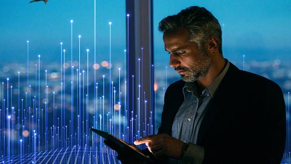 A businessman scrolling on a tablet by an office window