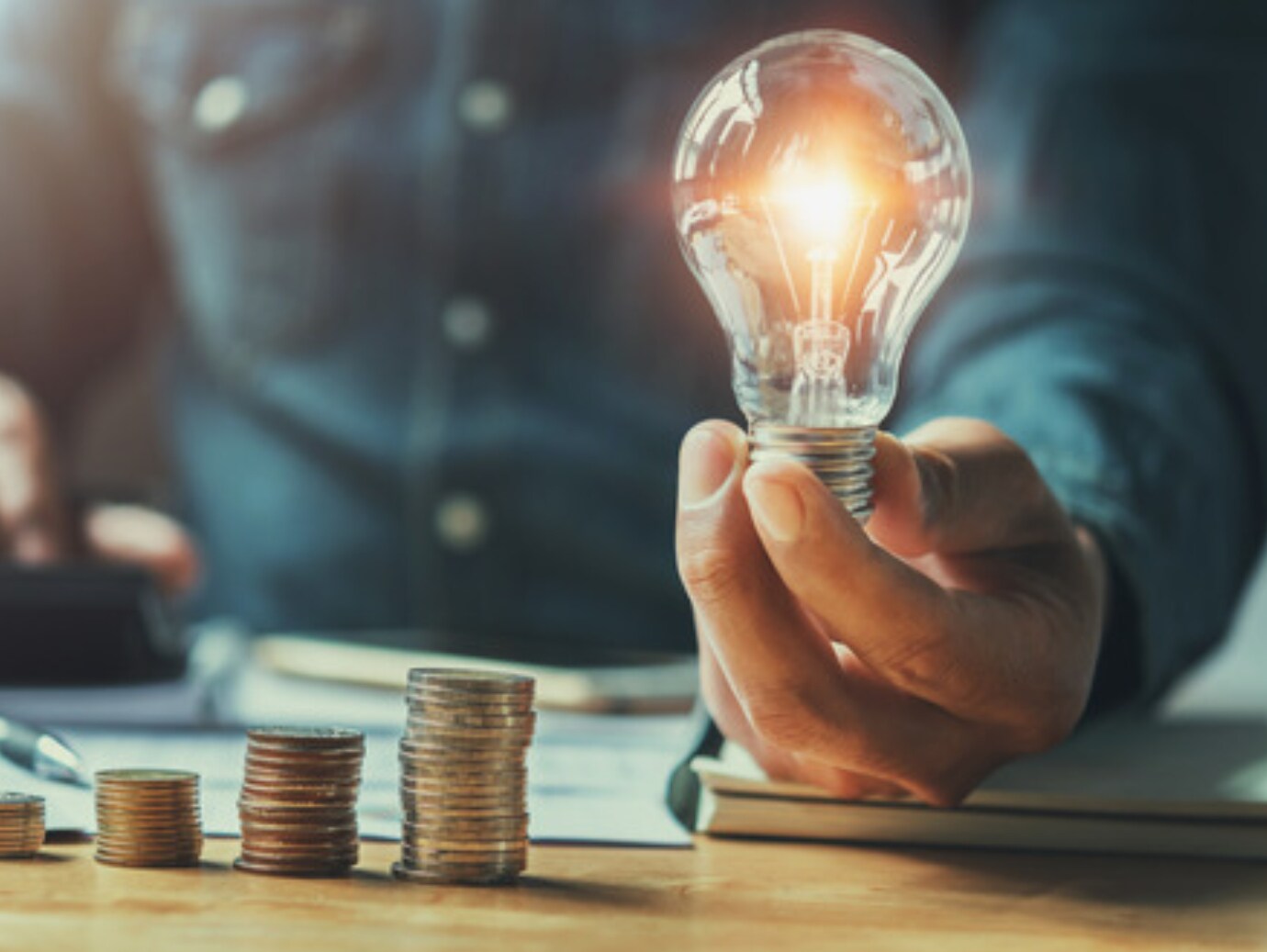 Man holding a light bulb with stacks of coins kept on a table