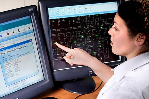 Woman working in front of two desktops side-by-side, while one displays the Simplex website