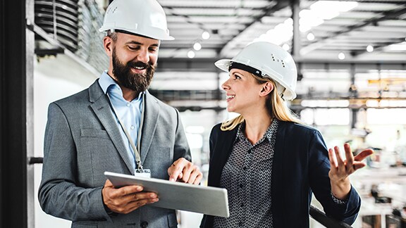 A person and person wearing hard hats looking at a tablet