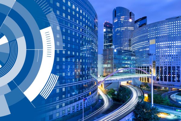 A view of corporate buildings in a city at dusk, with graphics depicting Digital Twinning overlaid on the left