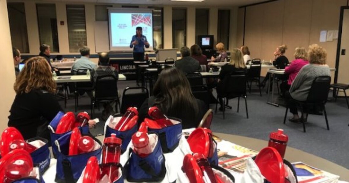 Women seated at a seminar hosted by Johnson Controls and Lincoln Tech, with several gift bags in the corner