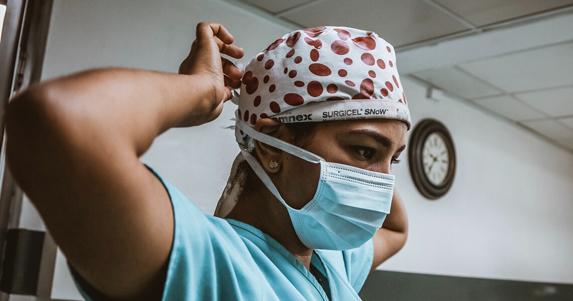 A doctor in scrubs tying a surgical cap