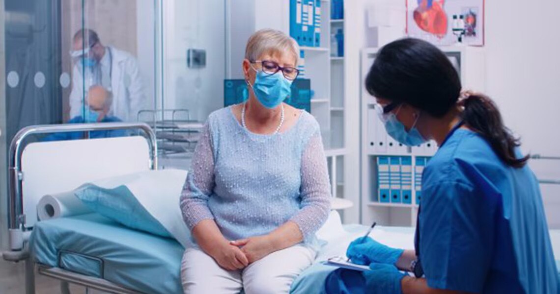 An elderly patient sitting up in bed and watching a nurse writing