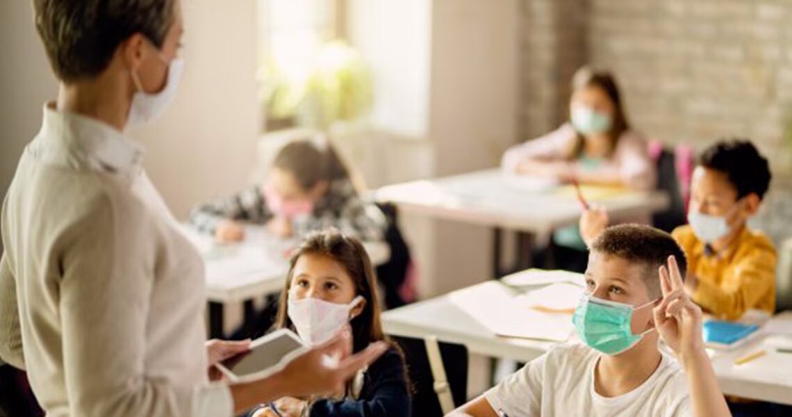 Teacher teaching elementary students in a classroom, where a boy has his hand raised