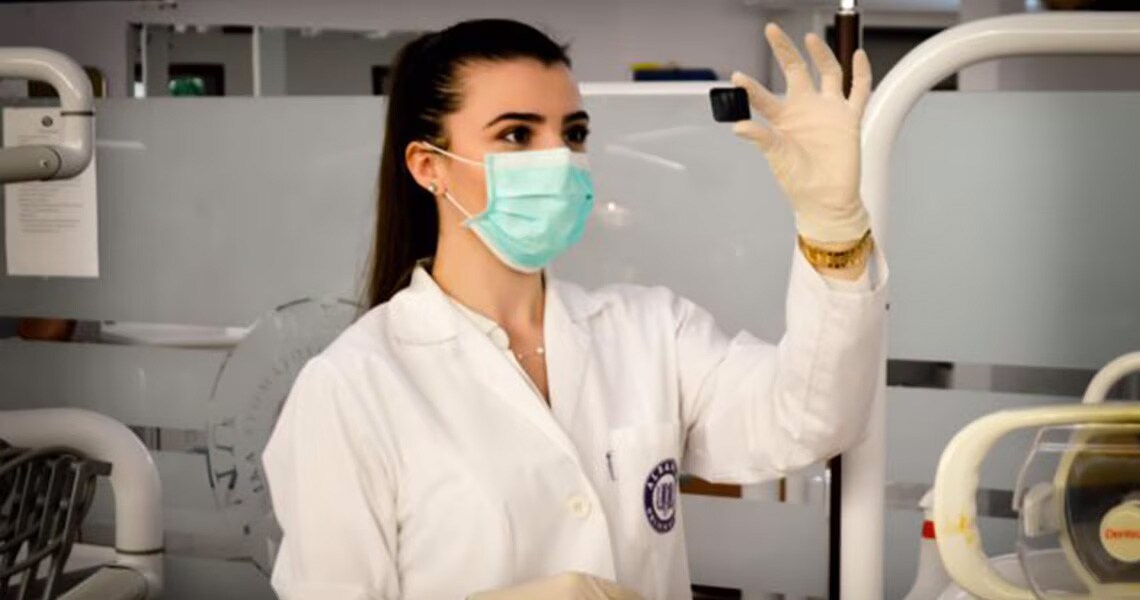 A female doctor wearing lab gear and a face-mask, holding up an X-ray of a tooth