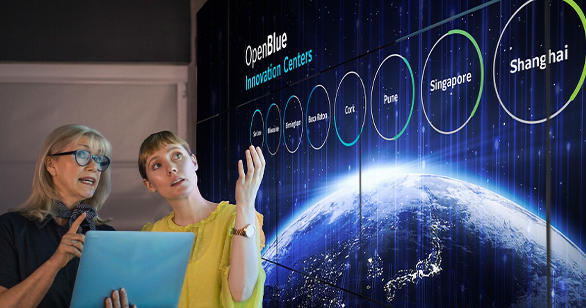 Two women next to a wall displaying details of OpenBlue Innovation Centres