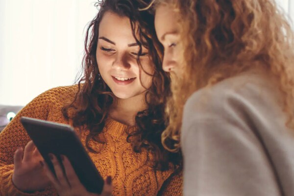 Two women sitting on a couch looking at a tablet