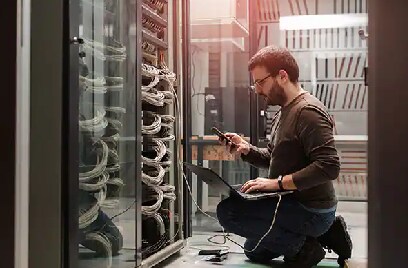 Man kneeling with a laptop in front of a data server rack