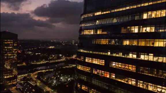 A corporate building lit up at dusk, with a cityscape behind