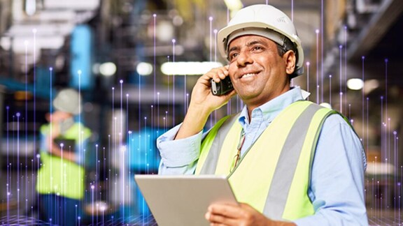 An engineer in protective gear holding a document and talking on a mobile