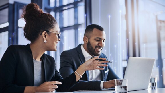 A woman in an office pointing at the laptop of the man seated beside her