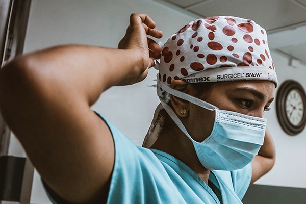 A doctor in scrubs tying a surgical cap