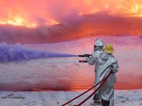 Two firefighters in safety suit dousing a flame using water hose